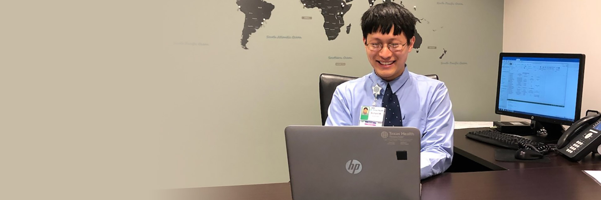 Academic Volunteer Sits behind desk in front of world map