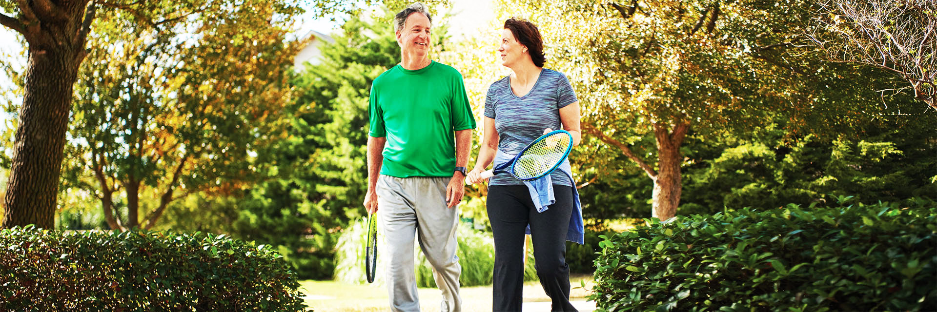 Couple walking outdoors holding tennis rackets