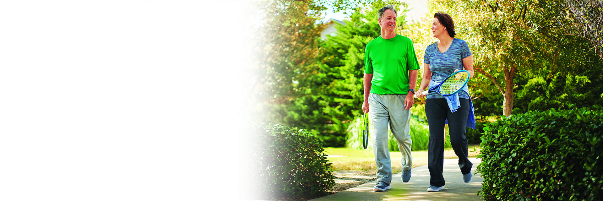 Couple walking outdoors holding tennis racquets