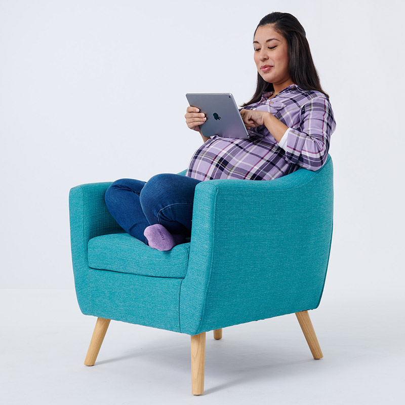Pregnant Woman sitting cross legged in chair holding iPad