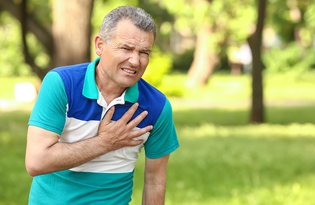 Mature man outdoors grabbing his chest