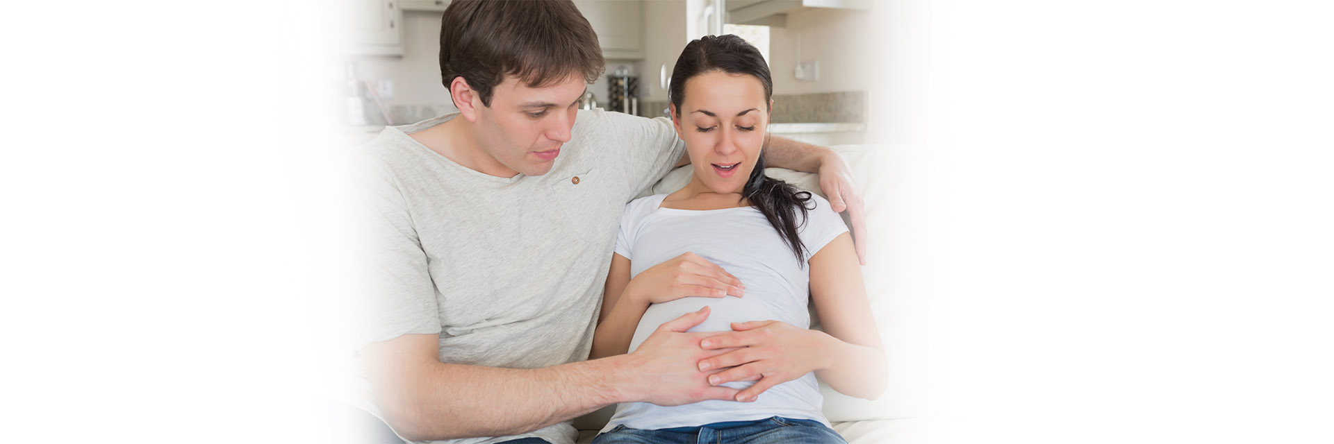 Young man on couch rubbing pregnant partners belly