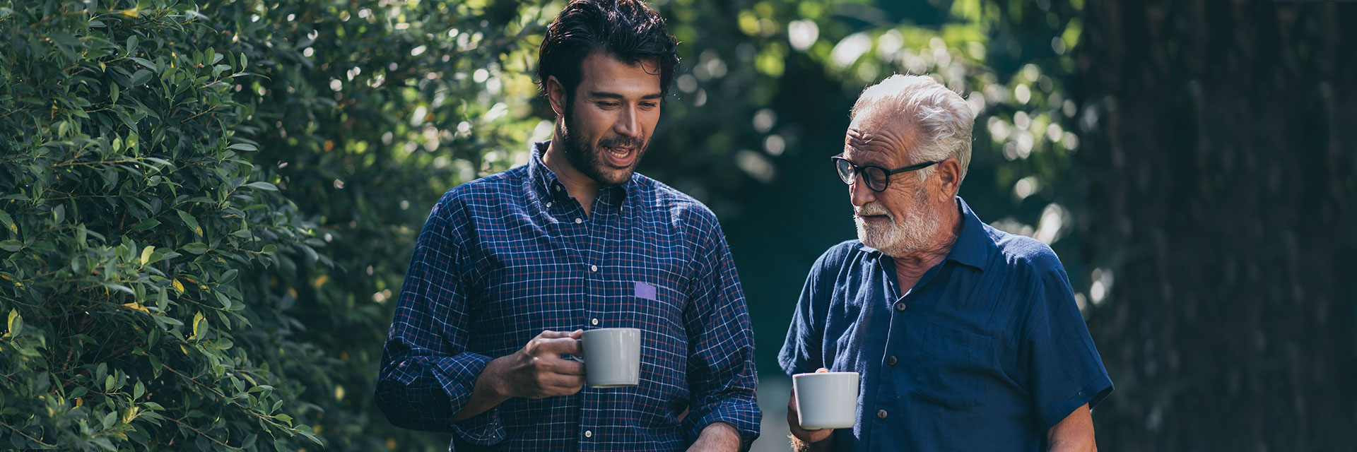 Older father and son holding mugs outdoors