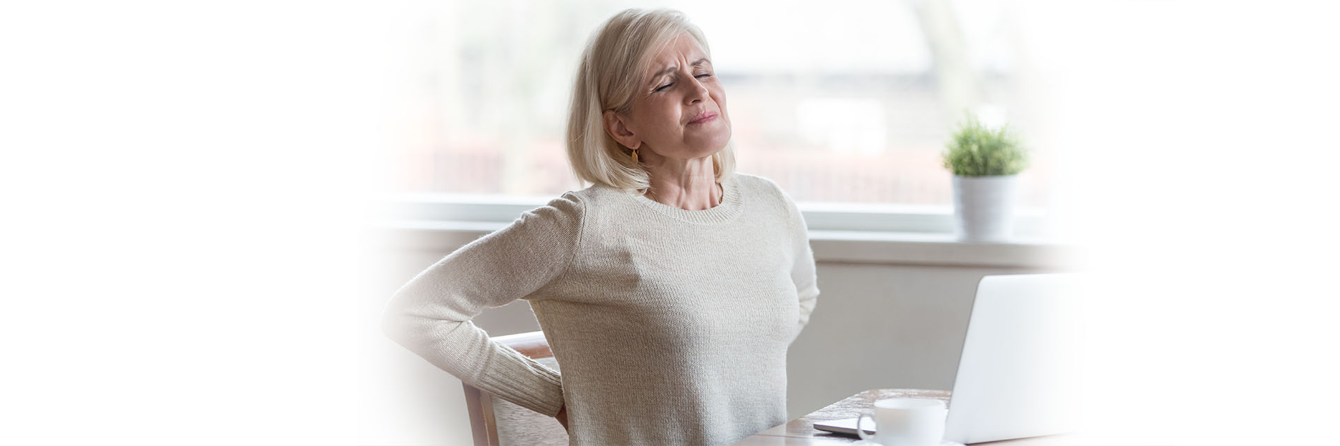 Woman sitting at a computer and hold her back