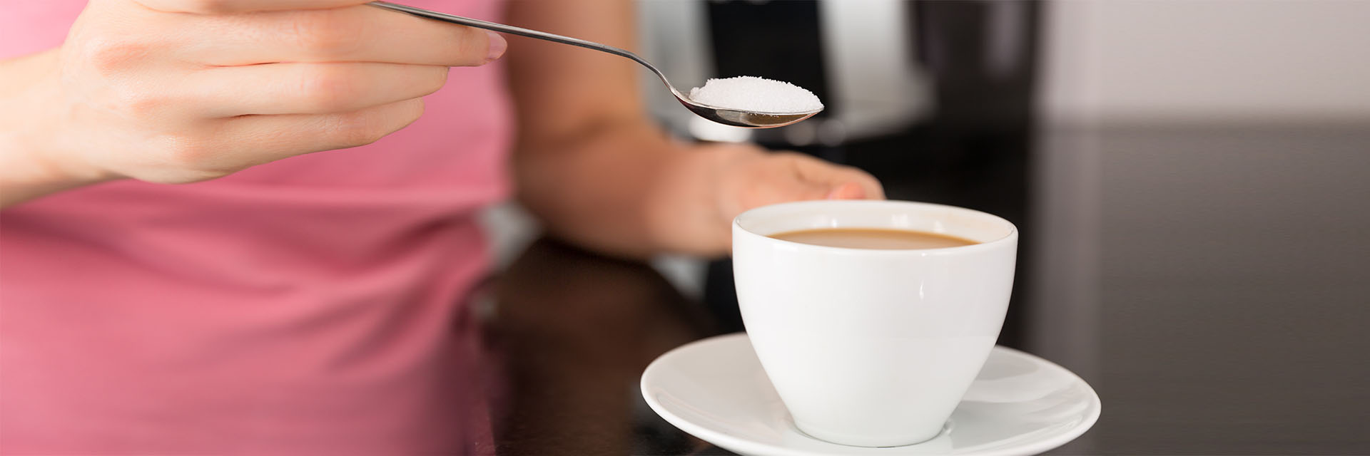 Woman's hand holding coffee cup and a spoonful of sweetener