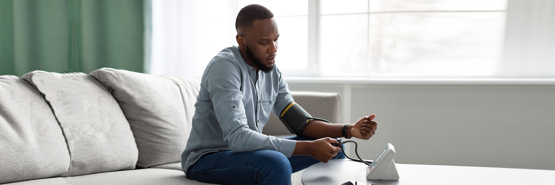 Man sitting on the couch taking his blood pressure using a cuff