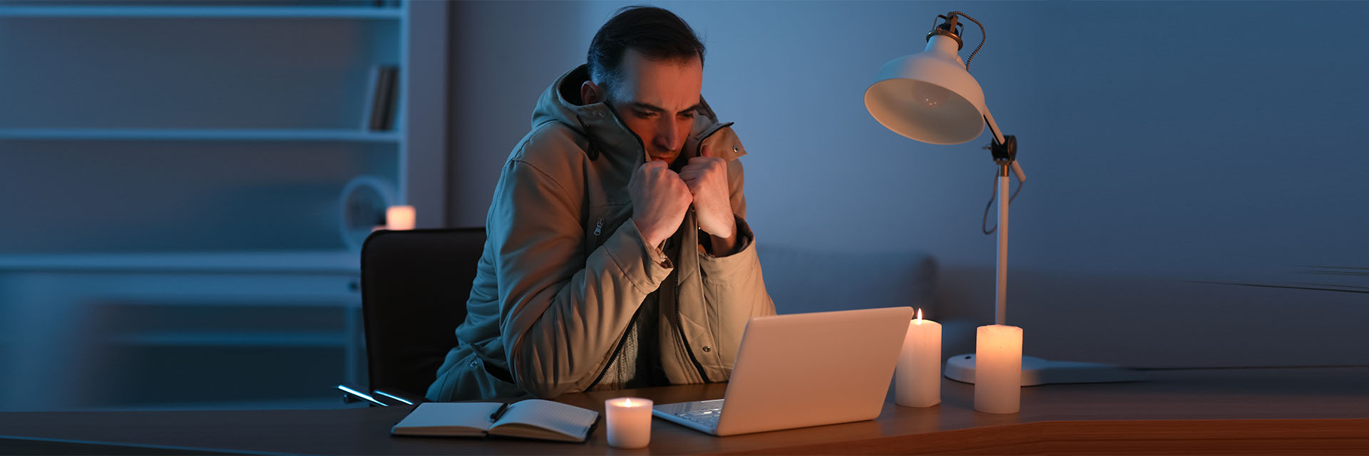 Man indoors working at a desk dressed in a coat