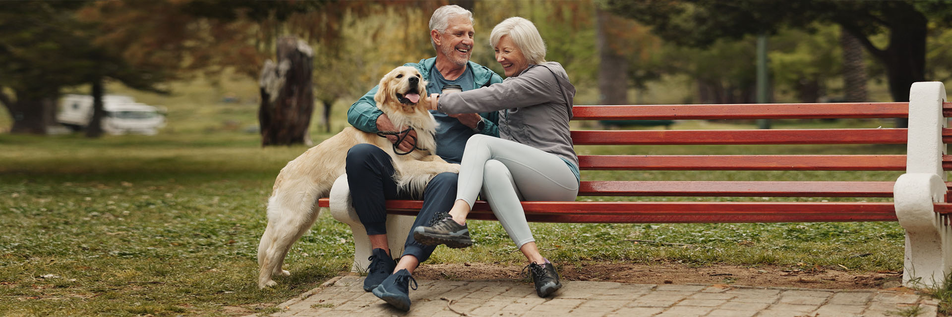 Mature man and woman sitting on a park bench playing with their dog