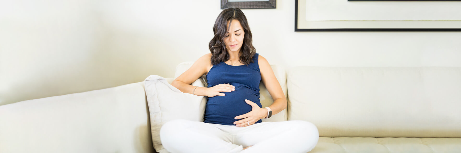 Pregnant woman sitting on the sofa holding her belly