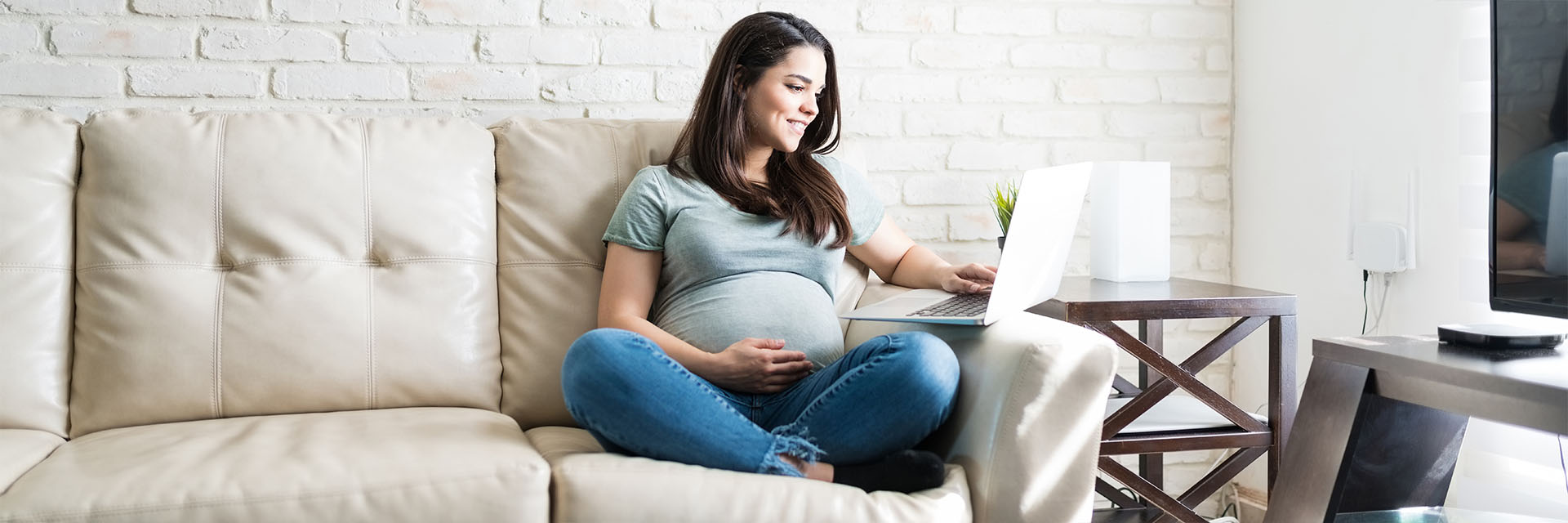 Pregnant woman sitting on the couch holding her laptop