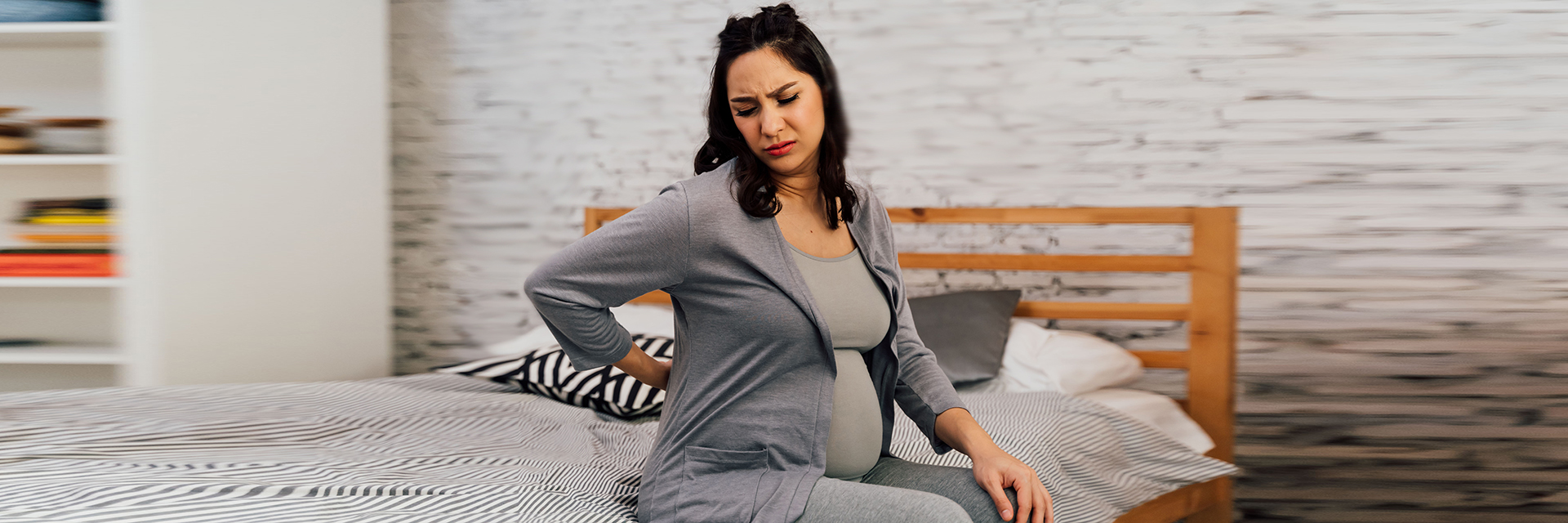 Pregnant woman sitting on the bed in pain