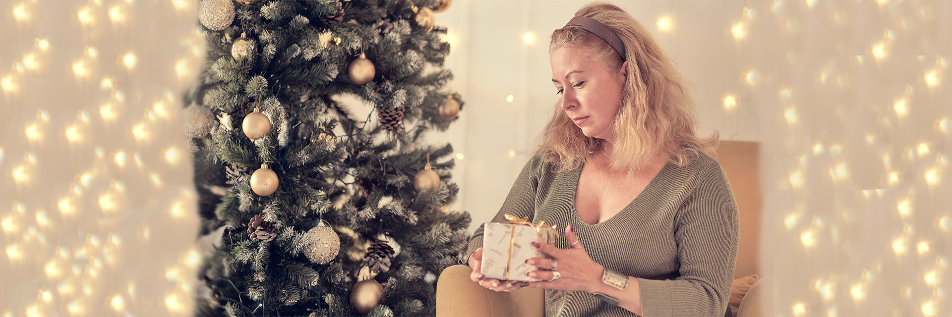Sad woman near a Christmas tree holding a small gift