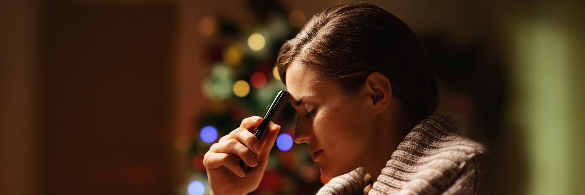 Woman holding hr head in front of a Christmas tree