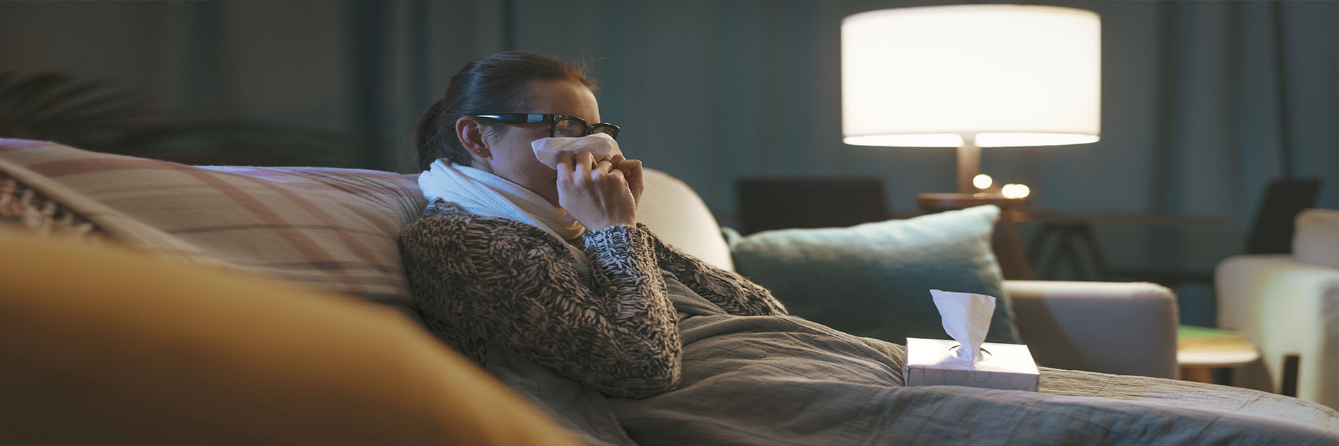 Woman on couch using tissue on her nose