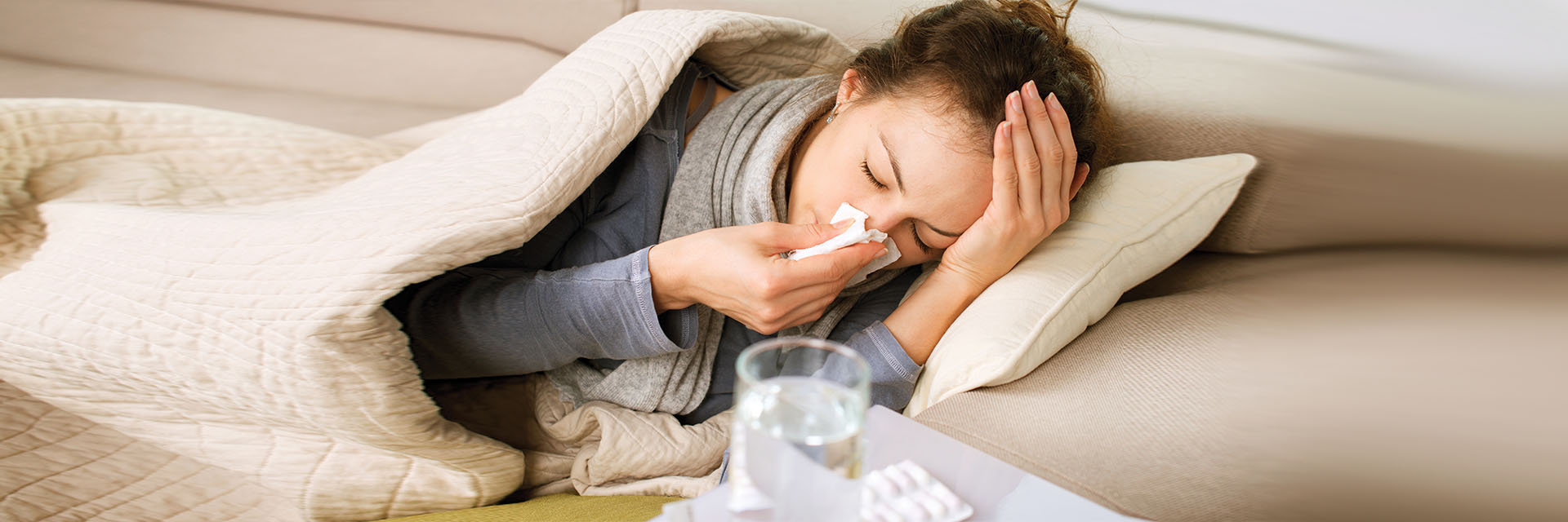 Woman sick on her couch wrapped in a blanket