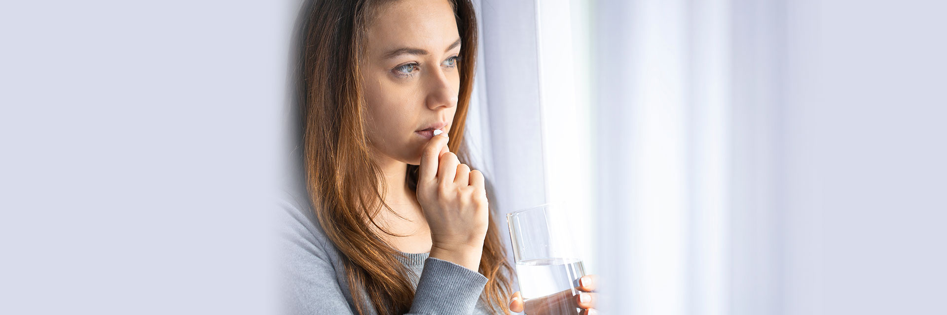 Woman taking a pill holding a glass of water