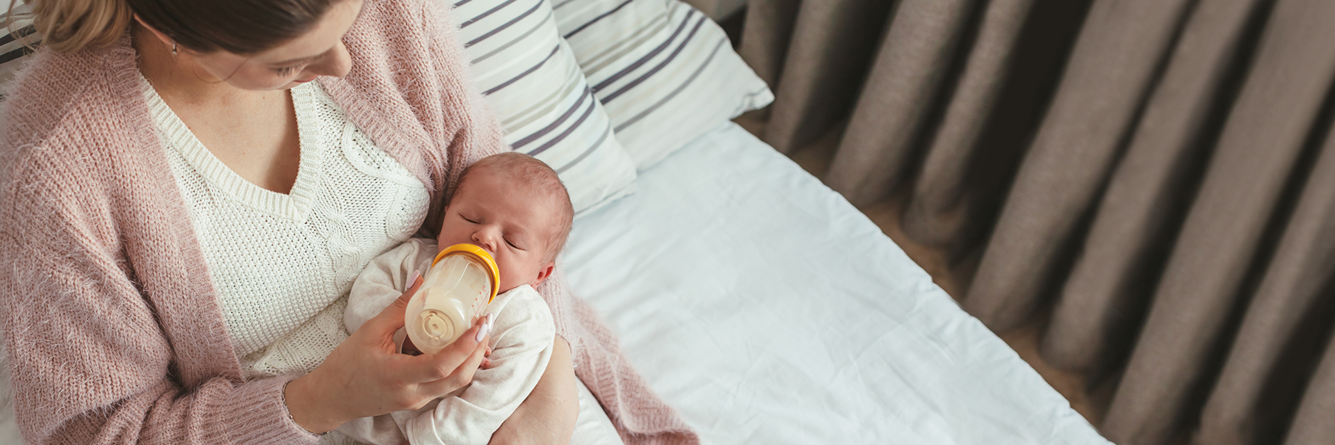 Mom feeding baby bottle in bed