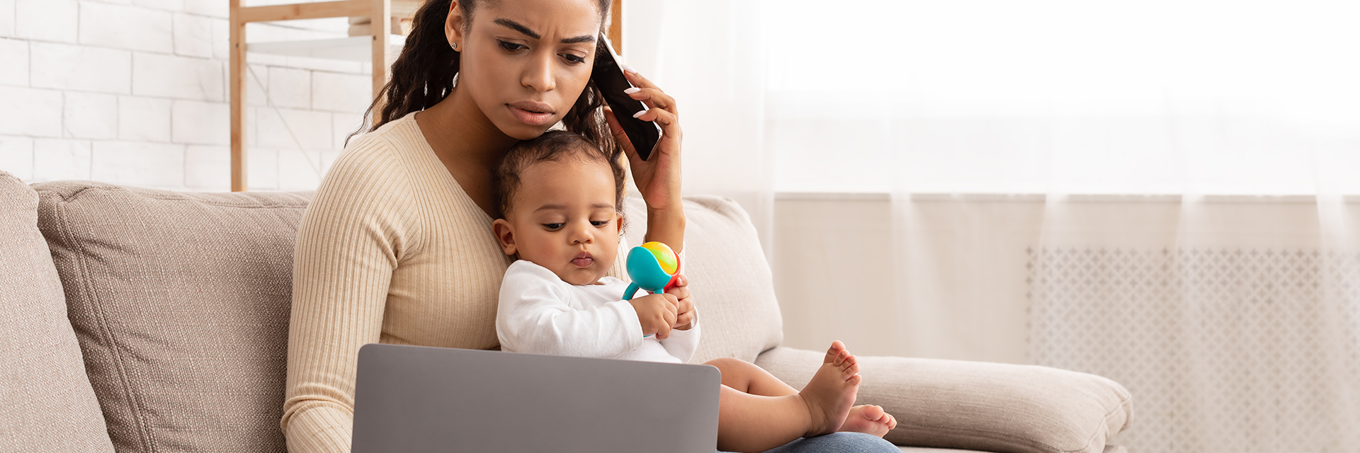 Mom holding baby on couch with laptop