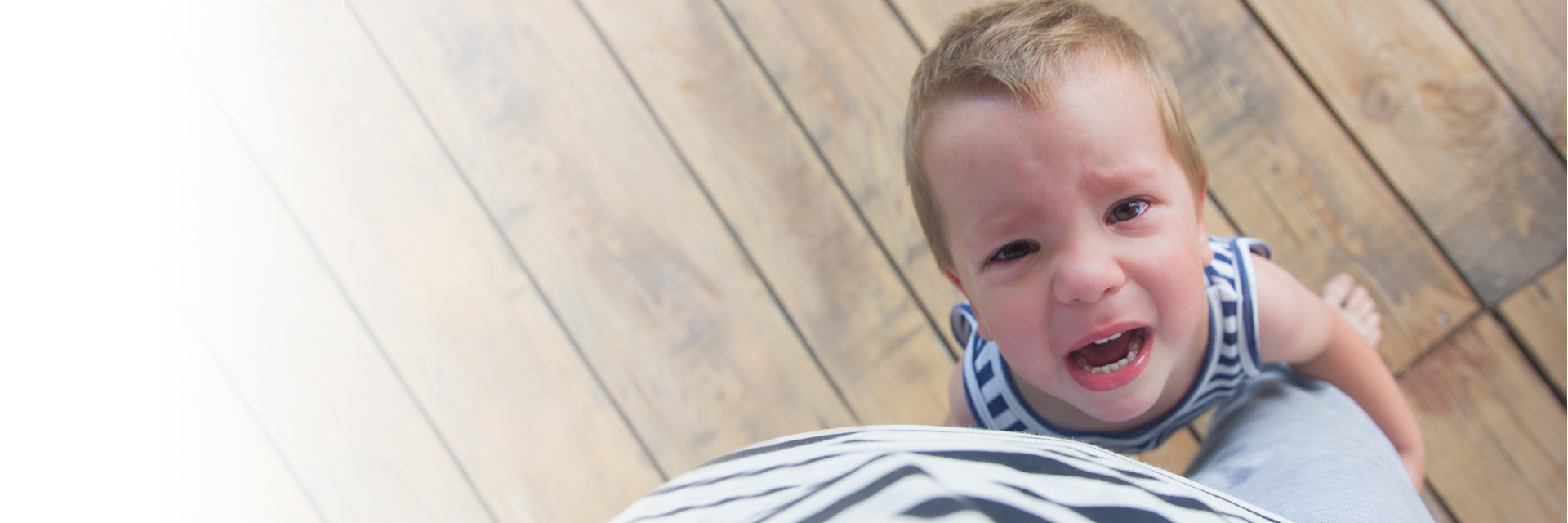 Crying boy holding parent leg