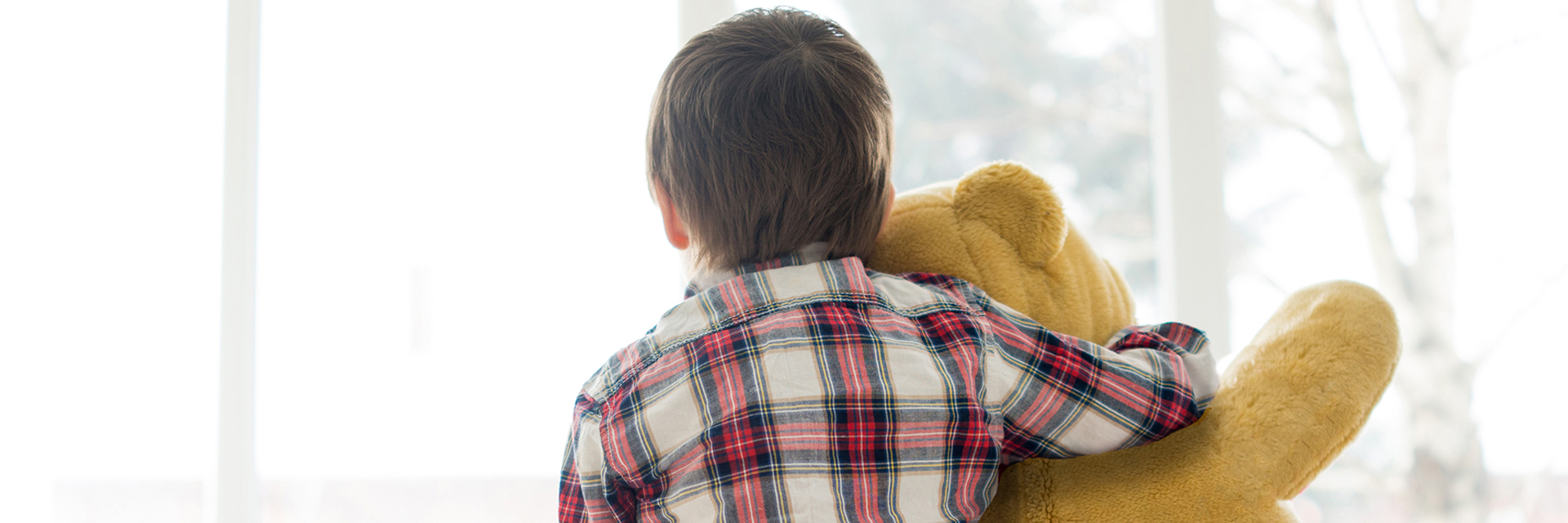 Little boy holding teddy bear near window