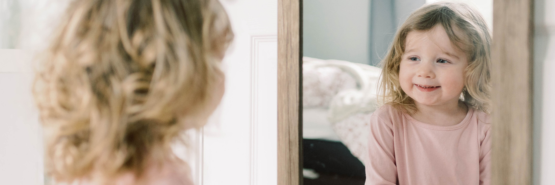 Little girl smiling at herself in mirror